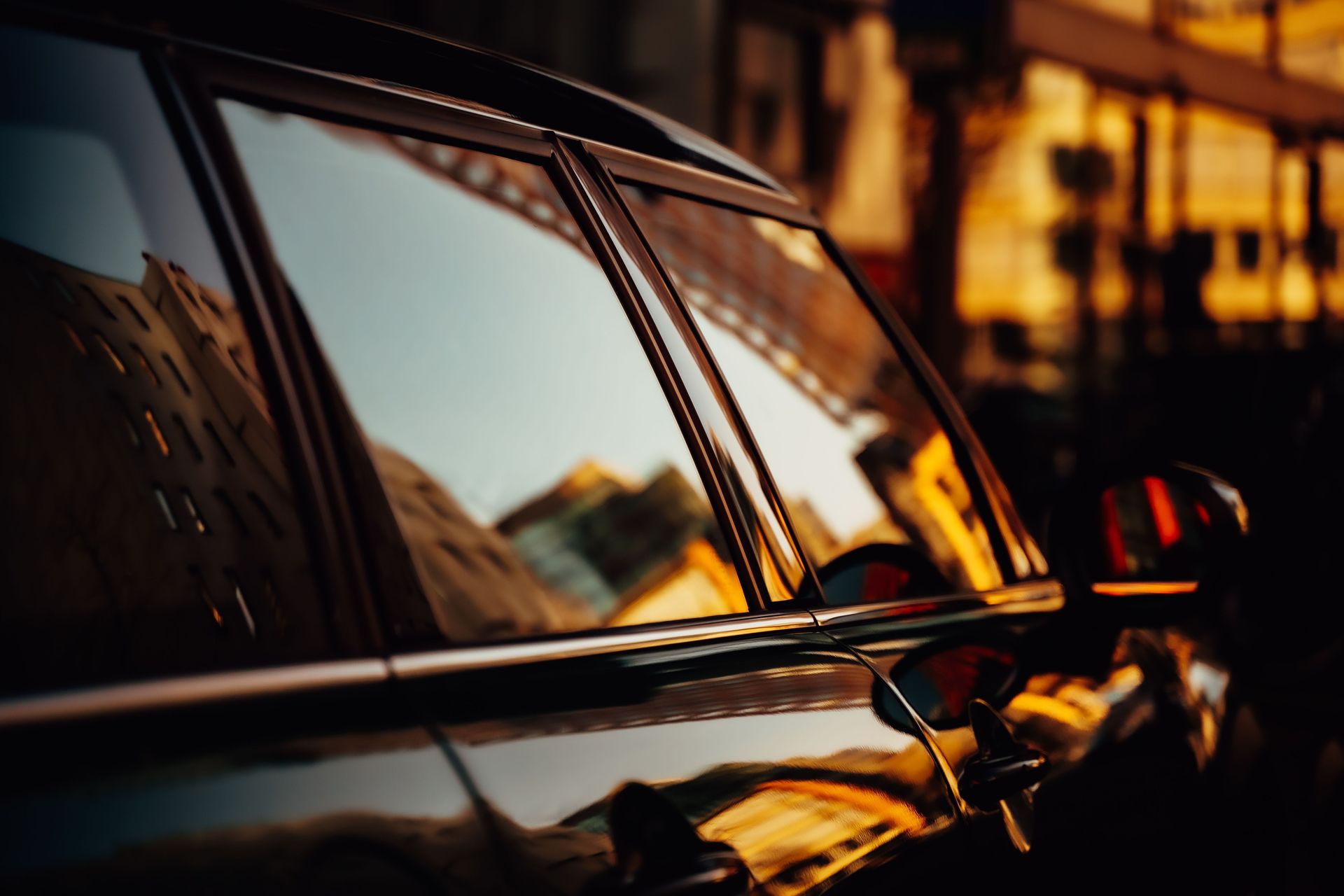 Close-up of a car window reflecting city buildings during sunset, captured with artistic flair.