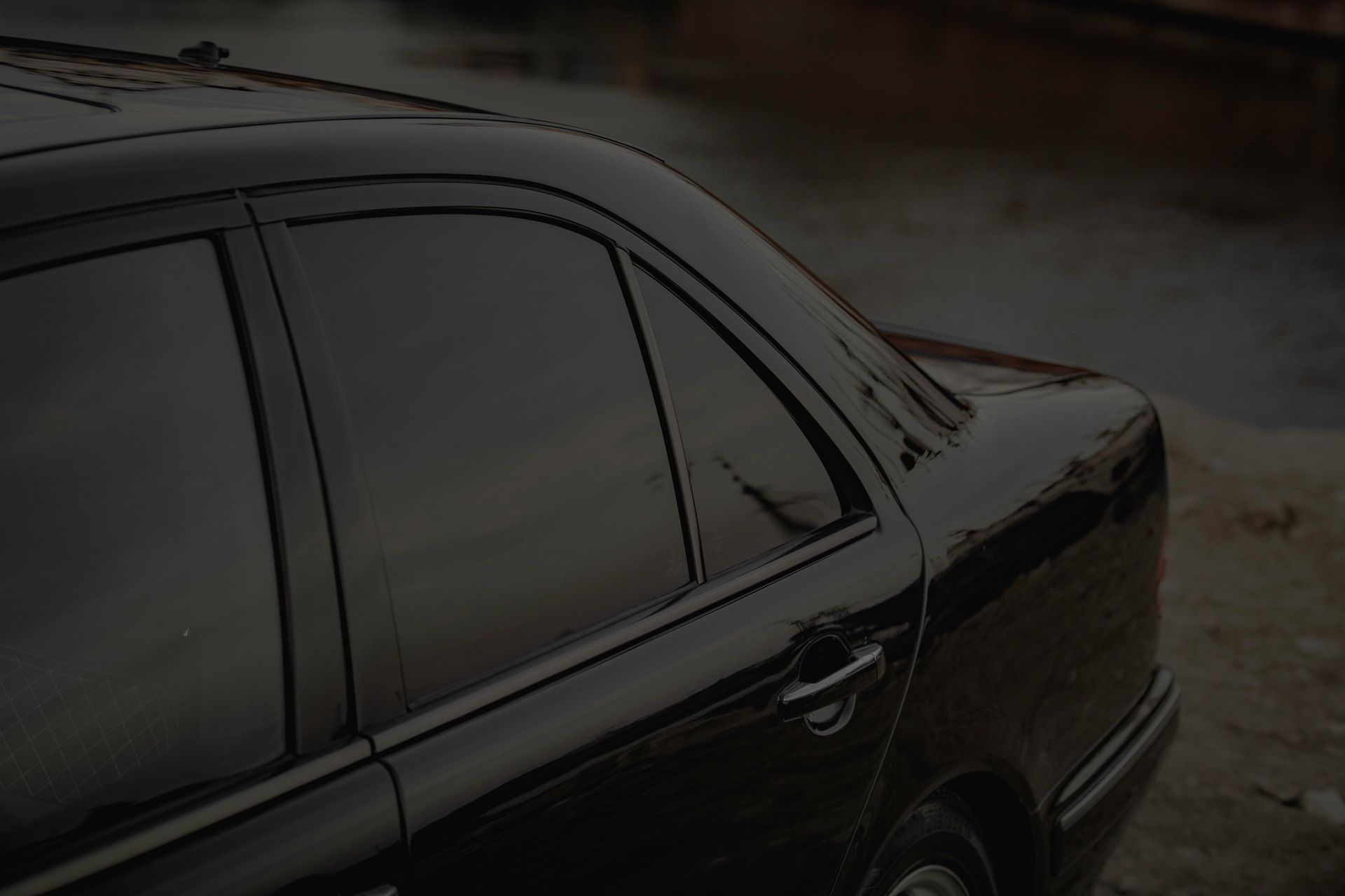 Close-up of a black car's side view with tinted windows by a calm riverbank.